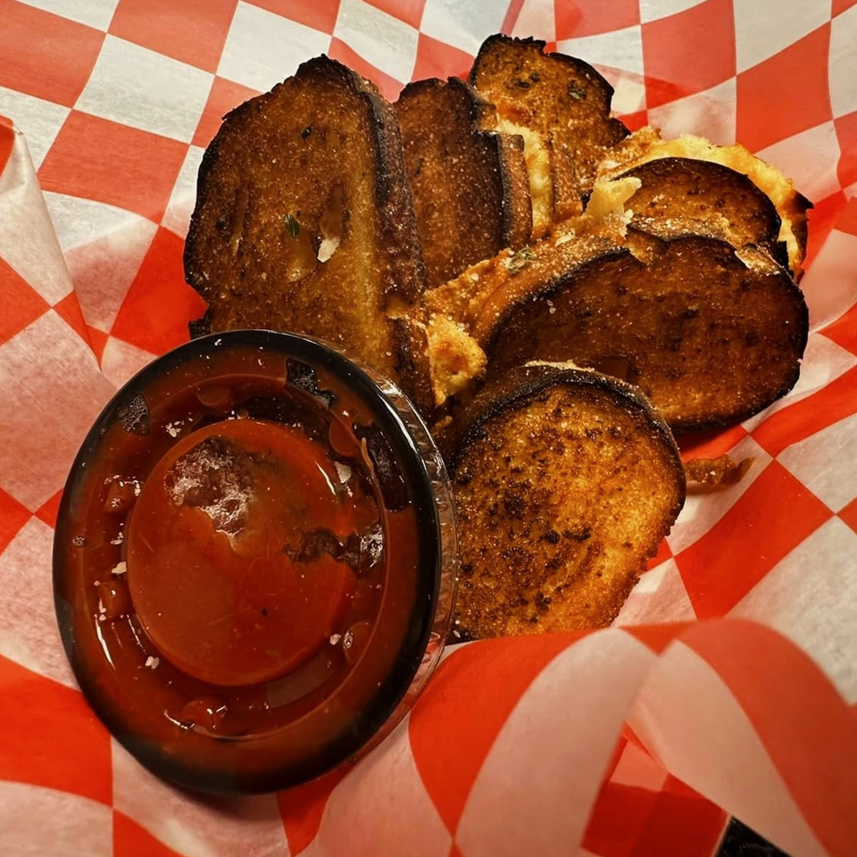 Toasted garlic bread slices with parmesan cheese and a side of marinara sauce in a red and white checkered basket.