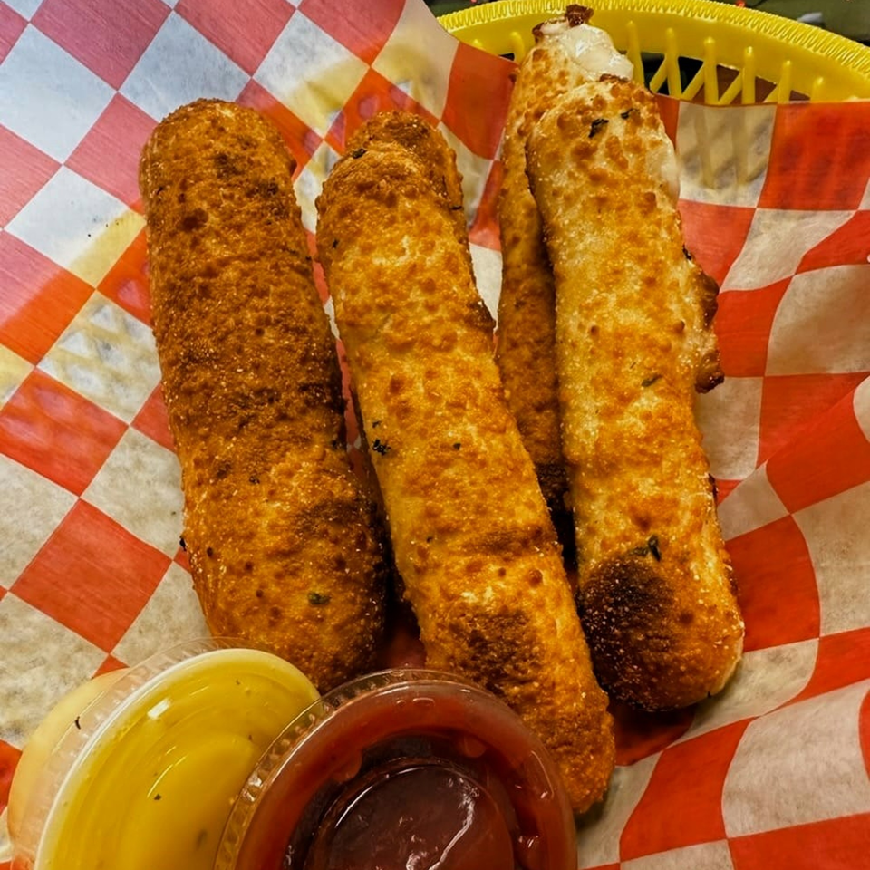 Golden-brown mozzarella sticks in a red and white checkered basket with two dipping sauces.