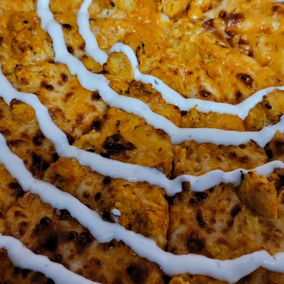 Close-up of Caprigios Pizza's cheesy bread with white garlic sauce drizzled on top.