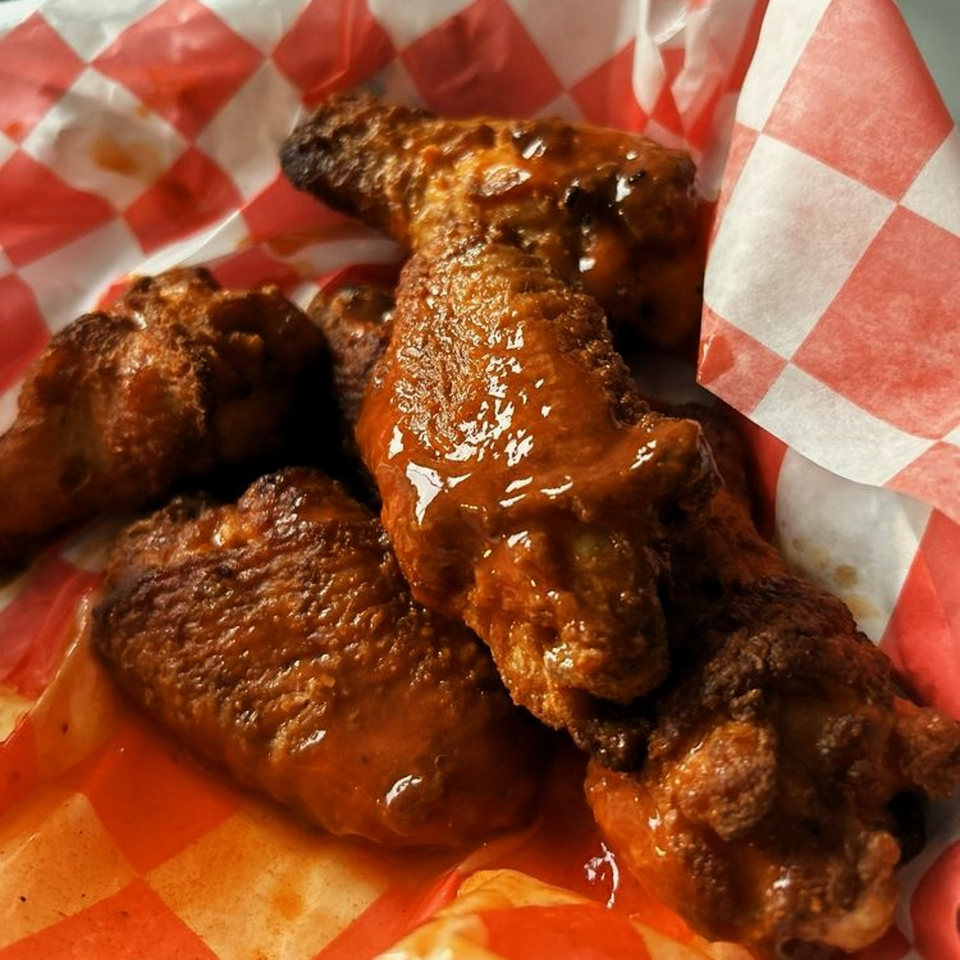 Caprigios Pizza's saucy chicken wings rest on red and white checkered paper.